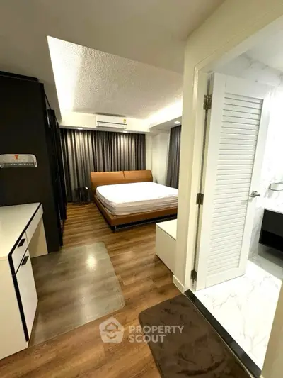 Modern bedroom with wooden flooring and adjacent bathroom in a stylish apartment.