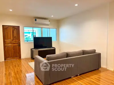 Spacious living room with modern sofa and large TV, featuring wooden flooring and ample natural light.