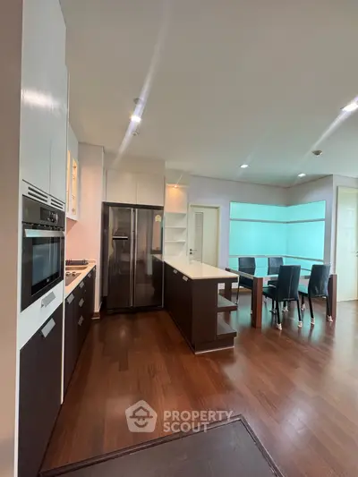 Spacious modern kitchen with open layout and dining area, featuring sleek appliances and elegant wooden flooring.