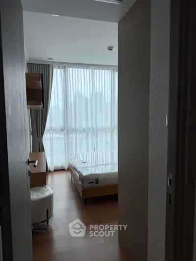 Modern bedroom with large windows and city view, featuring wooden flooring and minimalist furniture.