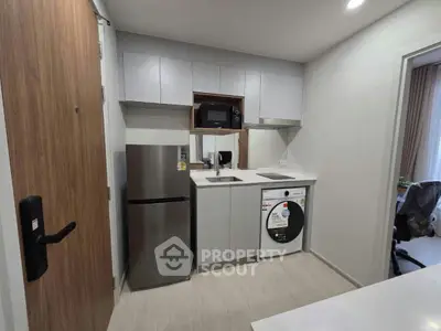 Modern compact kitchen with stainless steel appliances and washing machine in sleek apartment.