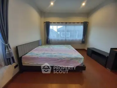 Spacious bedroom with large windows and elegant curtains, featuring a modern bed and wooden flooring.