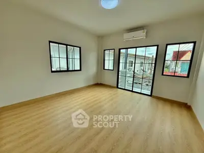 Spacious empty room with wooden flooring and large windows offering natural light.
