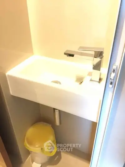 Compact bathroom sink with modern faucet and small trash bin underneath.