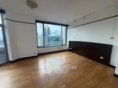 Spacious empty room with wooden flooring and large window offering stunning city view.