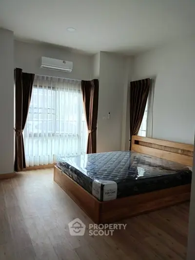 Spacious bedroom with wooden flooring and large window for natural light