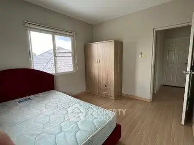 Cozy bedroom with natural light, featuring a comfortable bed and wooden wardrobe, perfect for relaxation.
