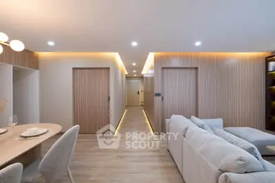 Modern living room with cozy seating and elegant dining area, featuring warm lighting and sleek wooden accents.