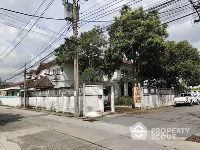 Charming corner house with lush trees and white walls in a serene neighborhood.