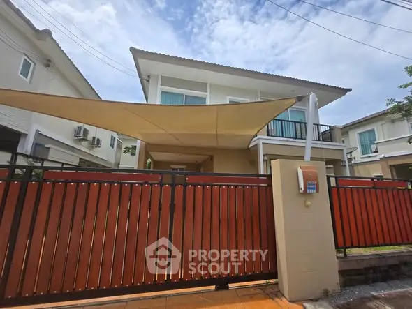 Modern two-story house with wooden fence and sunshade in suburban neighborhood.