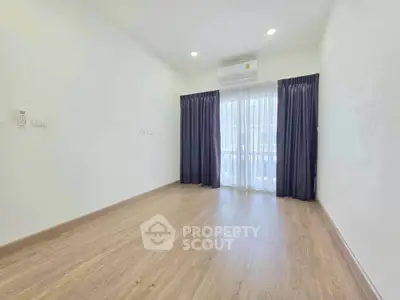 Spacious empty room with wooden flooring and large window, perfect for customization.