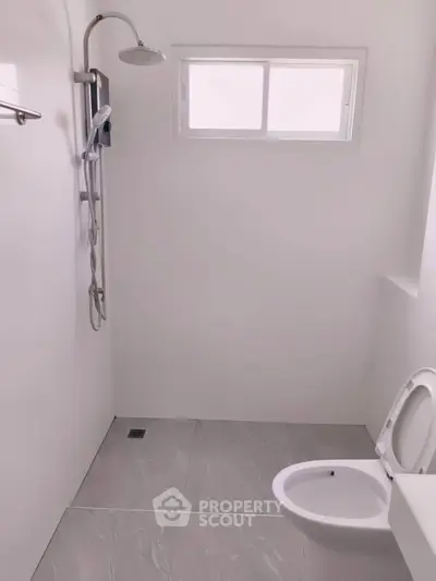 Minimalist bathroom with modern shower and toilet, featuring sleek white tiles and a small window for natural light.