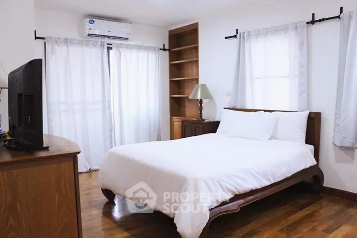 Cozy bedroom with wooden flooring, elegant bed, and natural light from large windows.