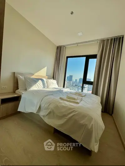 Modern bedroom with city view and natural light, featuring a cozy bed and elegant decor.