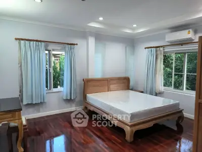Spacious bedroom with wooden flooring and large windows offering natural light.