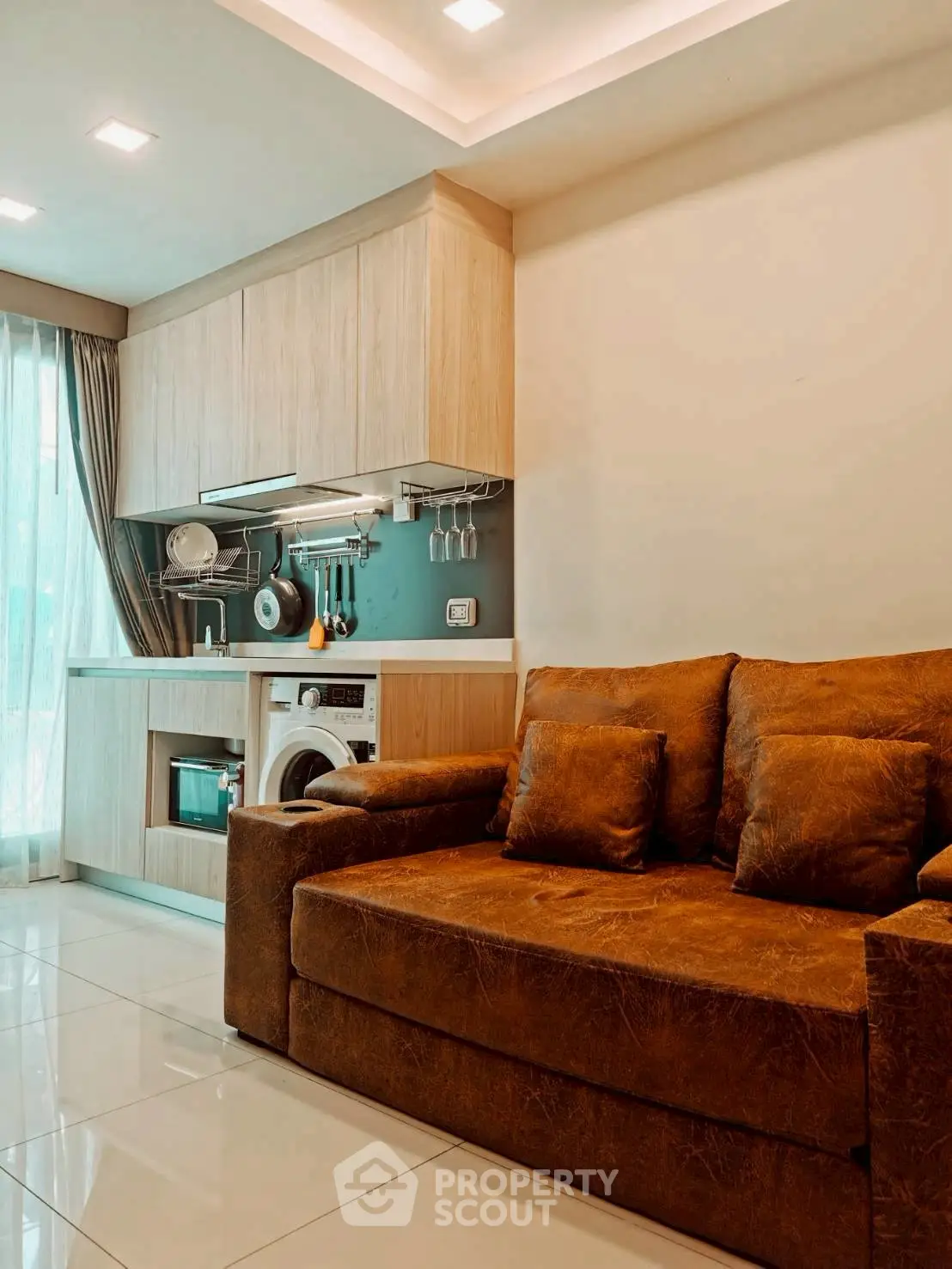 Modern living room with integrated kitchen and washing machine, featuring cozy brown sofa and sleek cabinetry.