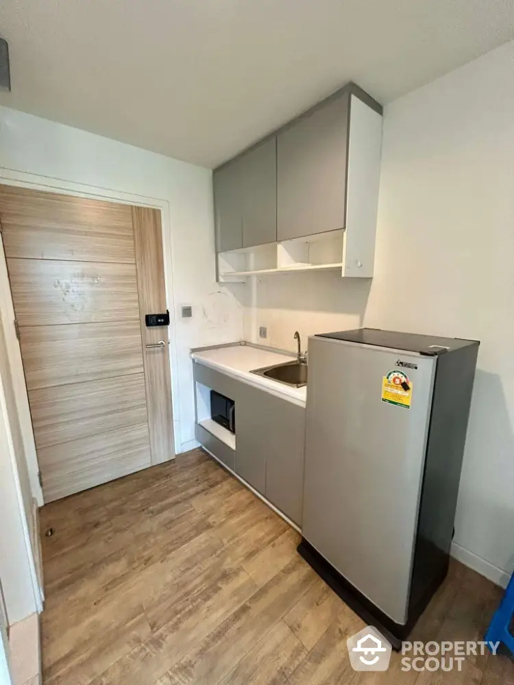 Compact kitchen with modern cabinetry and sleek refrigerator in cozy apartment.