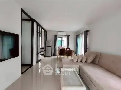 Modern living room with sleek design and open dining area, featuring a cozy sofa and large windows.
