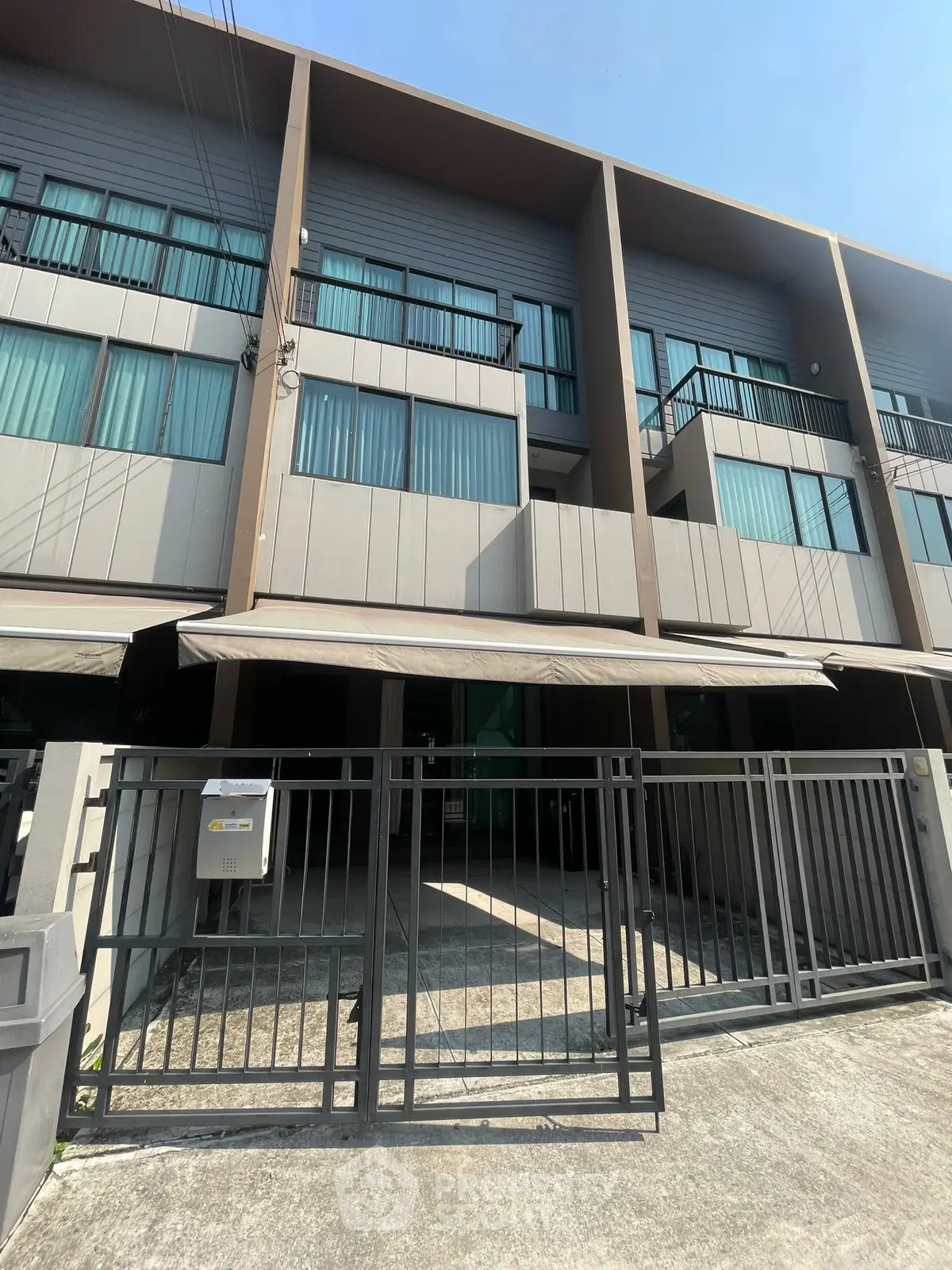 Modern townhouse exterior with gated entrance and balconies in a sunny neighborhood.