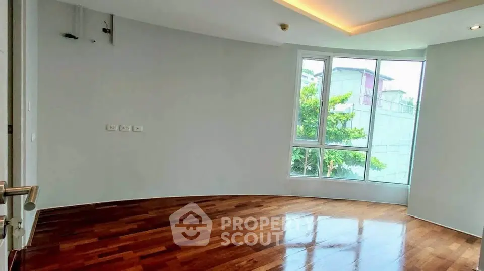 Spacious empty room with wooden floors and large window offering natural light.