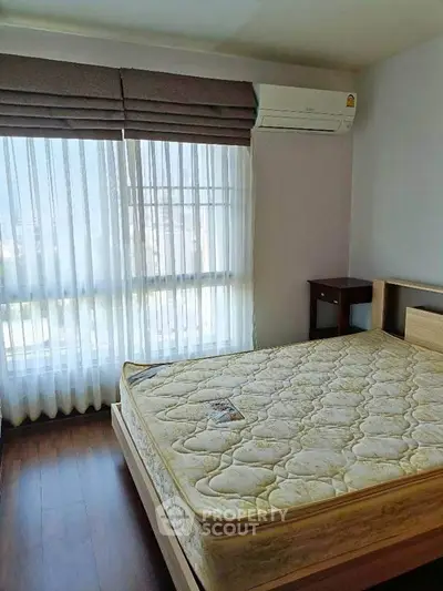 Bright bedroom with large window and air conditioning unit, featuring a comfortable bed.