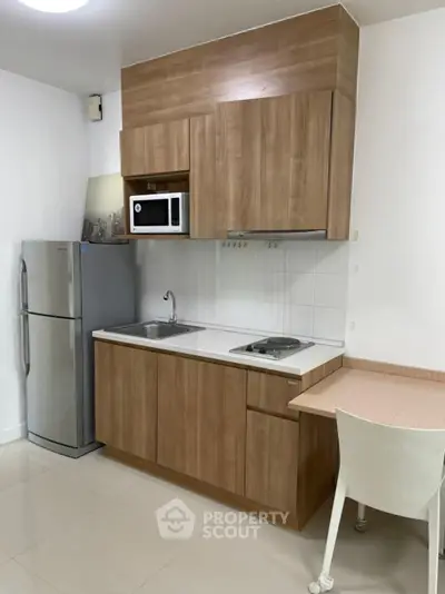Modern compact kitchen with wooden cabinets, stainless steel fridge, and built-in microwave.