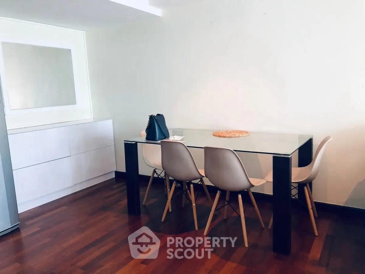 Modern dining area with sleek glass table and stylish chairs on wooden flooring.