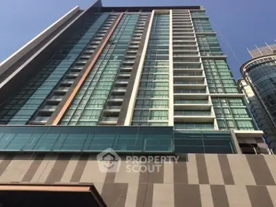 Modern high-rise building with glass facade and balconies in urban setting.