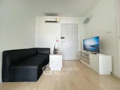 Modern living room with sleek black sofa and flat-screen TV, minimalist design.