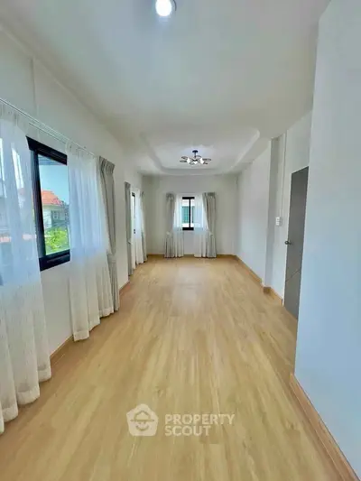 Spacious empty room with wooden flooring and large windows, perfect for customization.