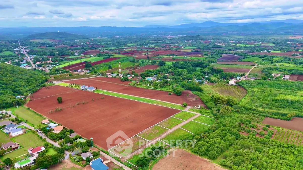 Expansive aerial view of lush agricultural land with scenic mountains in the background, ideal for development.