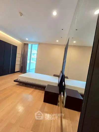Spacious modern bedroom with wooden flooring and large window for natural light.