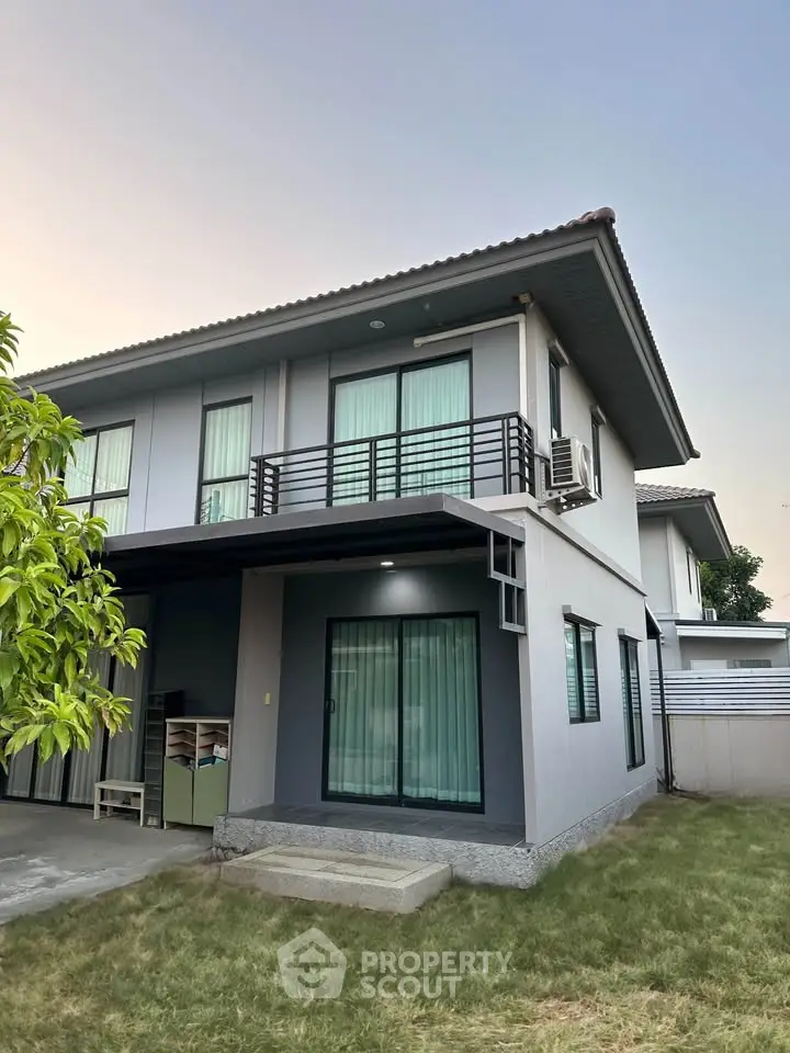 Modern two-story house with balcony and lush lawn in serene neighborhood.