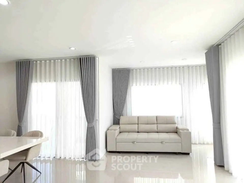 Bright and spacious living room with modern white sofa and elegant curtains.
