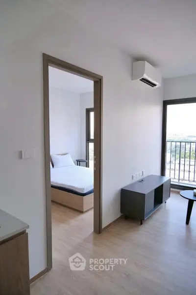 Modern apartment interior with bedroom and living area, featuring sleek furniture and natural light.