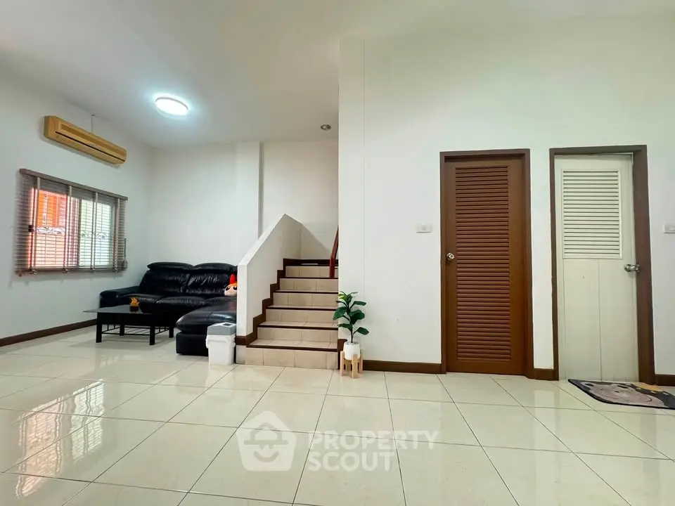 Spacious living room with modern staircase and sleek black sofa, perfect for family gatherings.