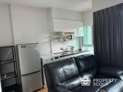 Modern compact kitchen with appliances and cozy black leather sofa in stylish apartment.