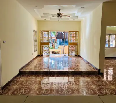 Spacious living room with decorative tiled flooring and ceiling fan, overlooking a garden view.