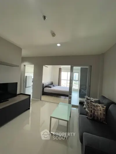 Modern living room with sleek furniture and open layout leading to a cozy bedroom.