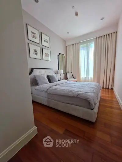 Elegant bedroom with wooden flooring, stylish decor, and natural light from large window.