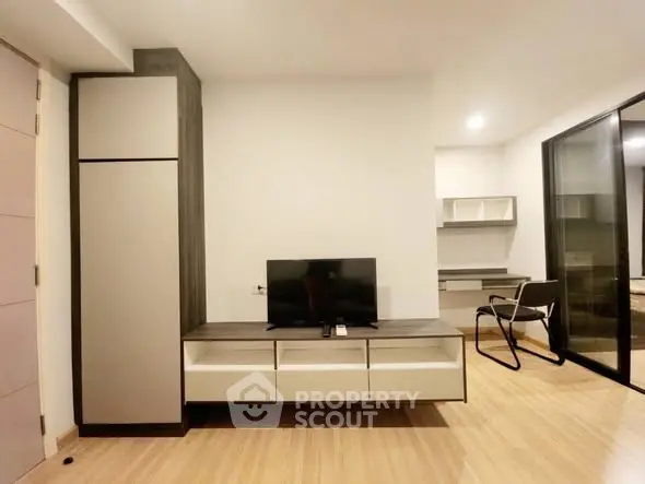 Modern living room with sleek furniture and open layout, featuring a TV and workspace.