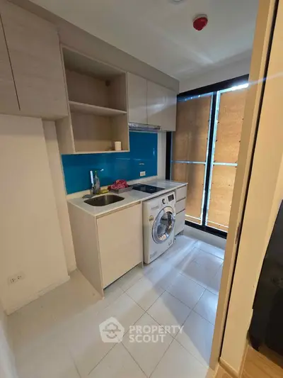Modern compact kitchen with washing machine and sleek cabinetry in a bright apartment.