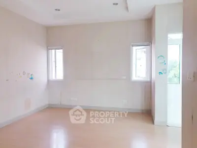 Spacious empty room with light wood flooring and two windows