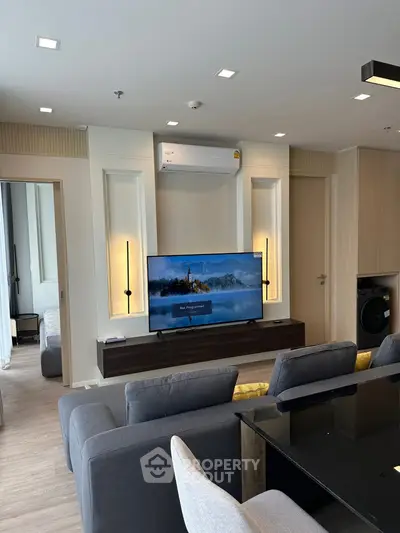 Modern living room with sleek furniture and large TV, open to a cozy bedroom.