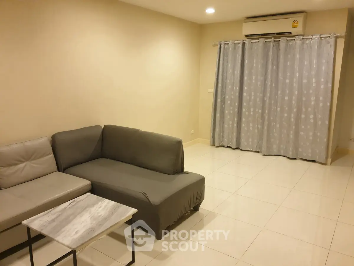 Spacious living room with modern sofa and air conditioning, ideal for relaxation.