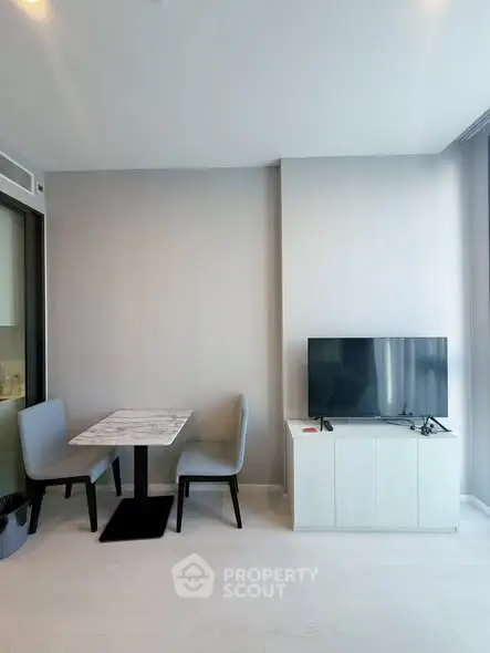 Modern living room with sleek furniture and natural light, featuring a TV and dining area.