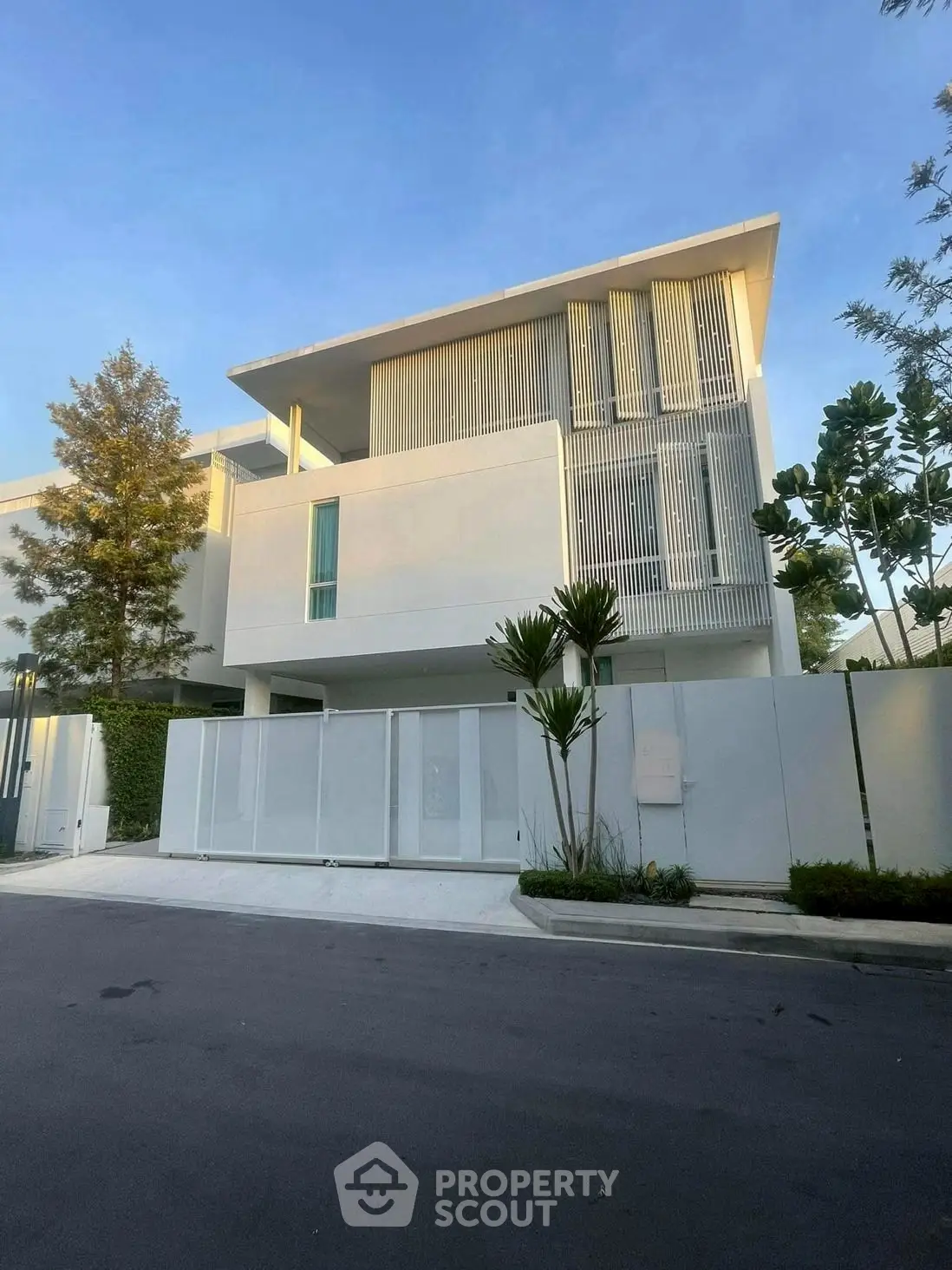 Modern minimalist white house with sleek design and lush greenery in upscale neighborhood.
