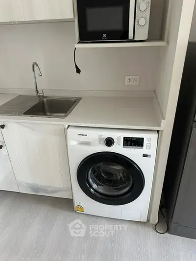 Modern kitchen with built-in washing machine and microwave, sleek cabinetry, and stainless steel sink.