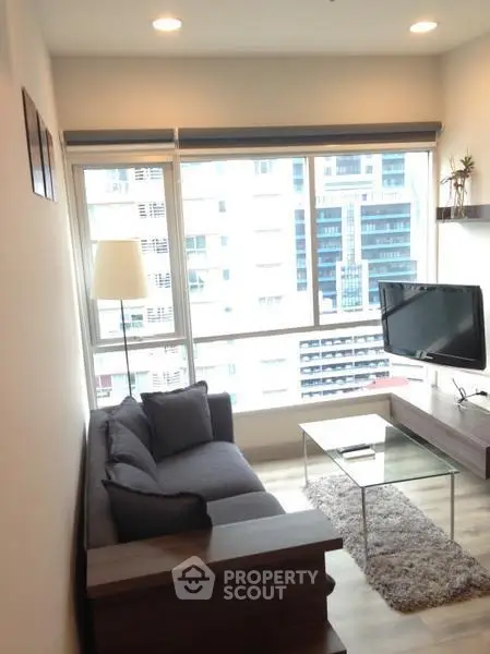 Modern living room with large windows and city view, featuring cozy sofa and wall-mounted TV.