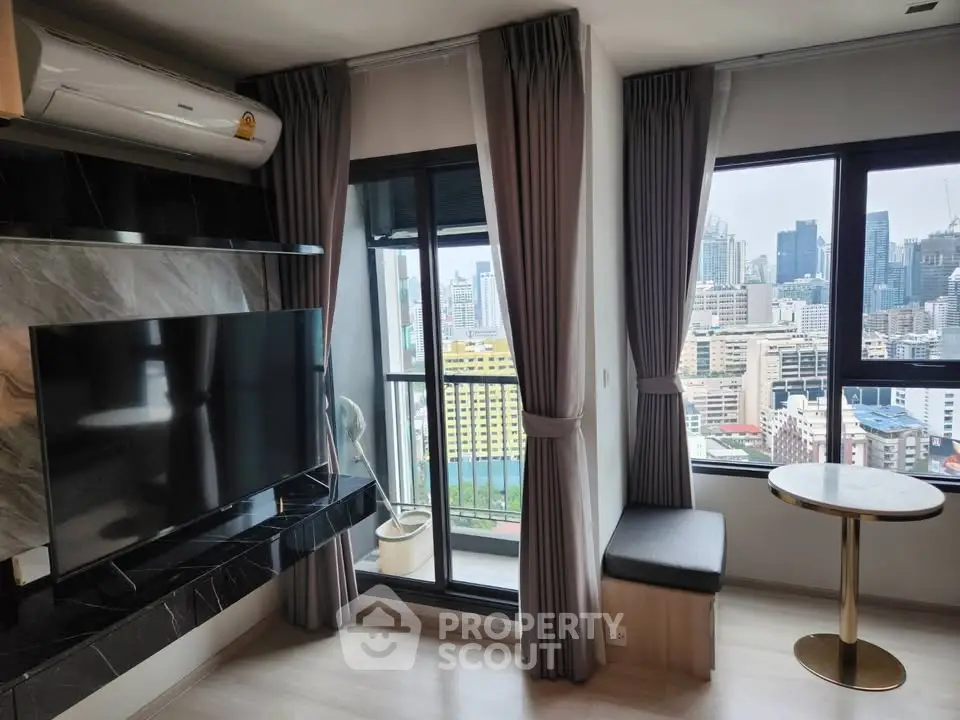 Modern living room with city view, featuring large windows, sleek TV setup, and cozy seating area.
